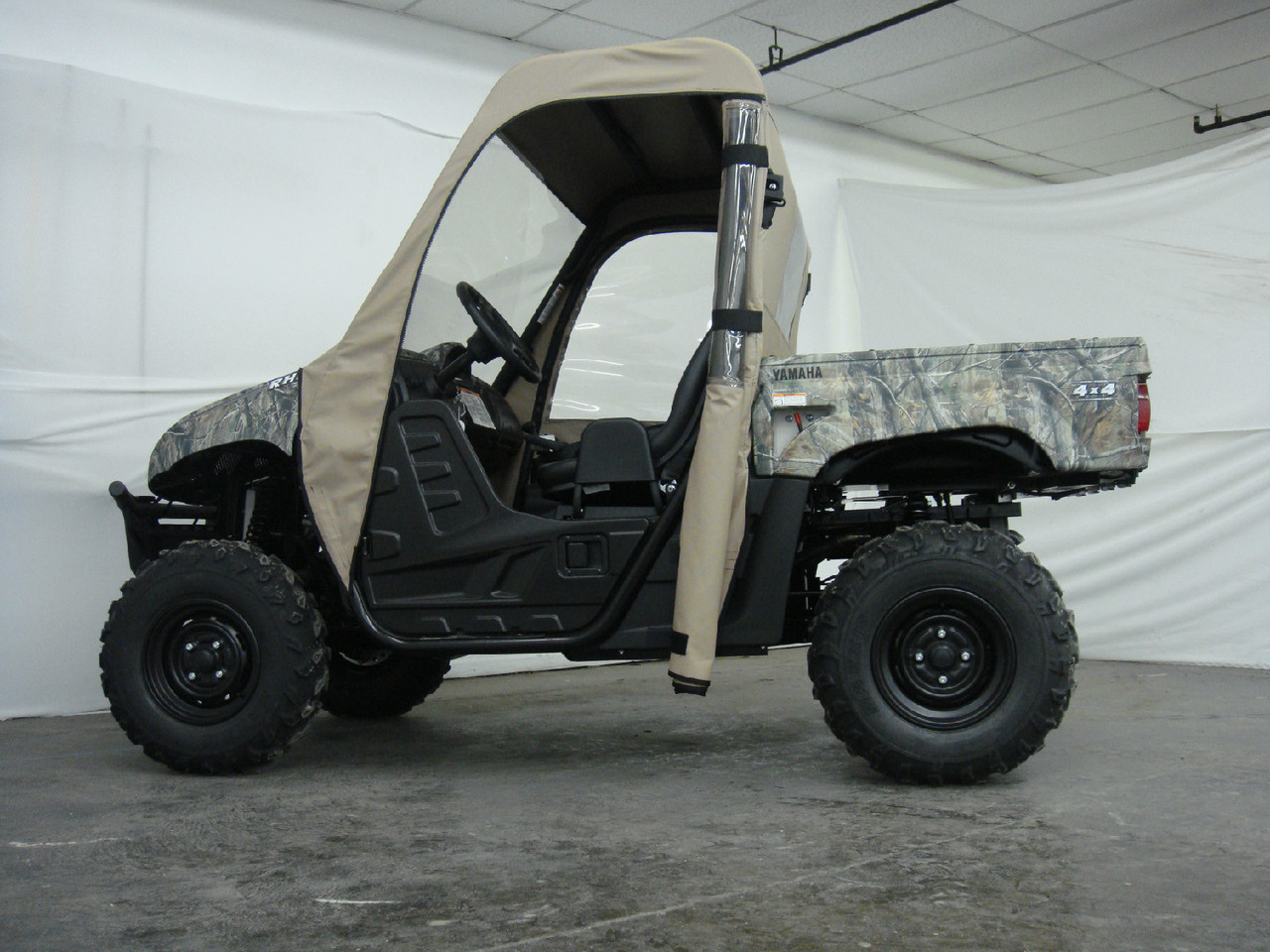 Side view of the camo Yamaha Rhino with the 3 Star tan cab enclosure door rolled up and tied open, showing the seats
