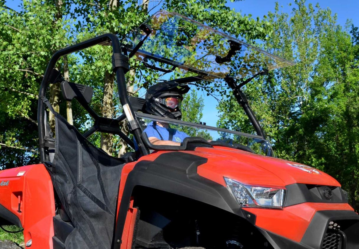 SuperATV flip-up windshield with the top half open on a red Kymco UXV 450, helmeted driver seated, front angle view