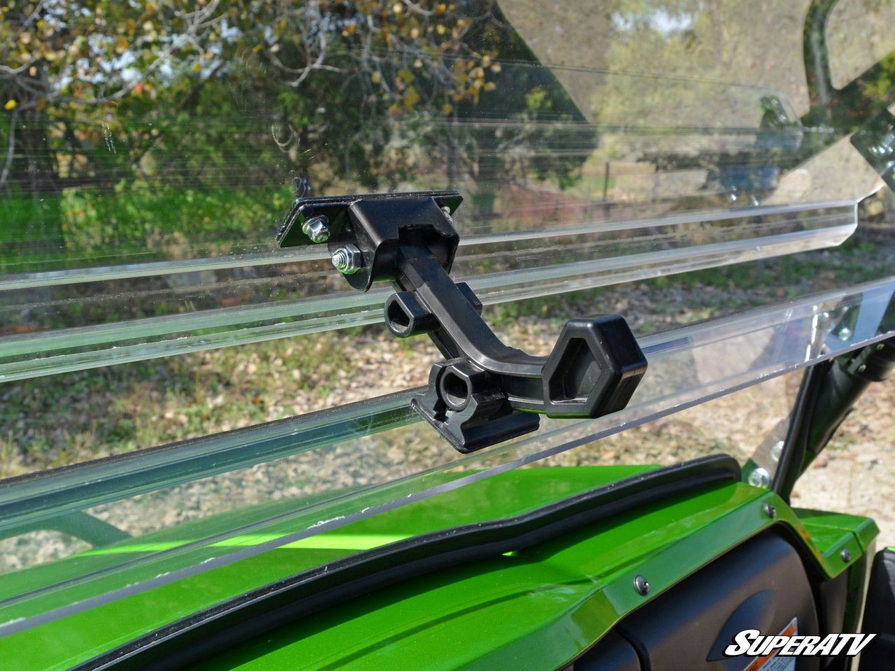 Close-up of the black latch clamp on the SuperATV flip windshield hinge above the green Kawasaki Teryx4 hood