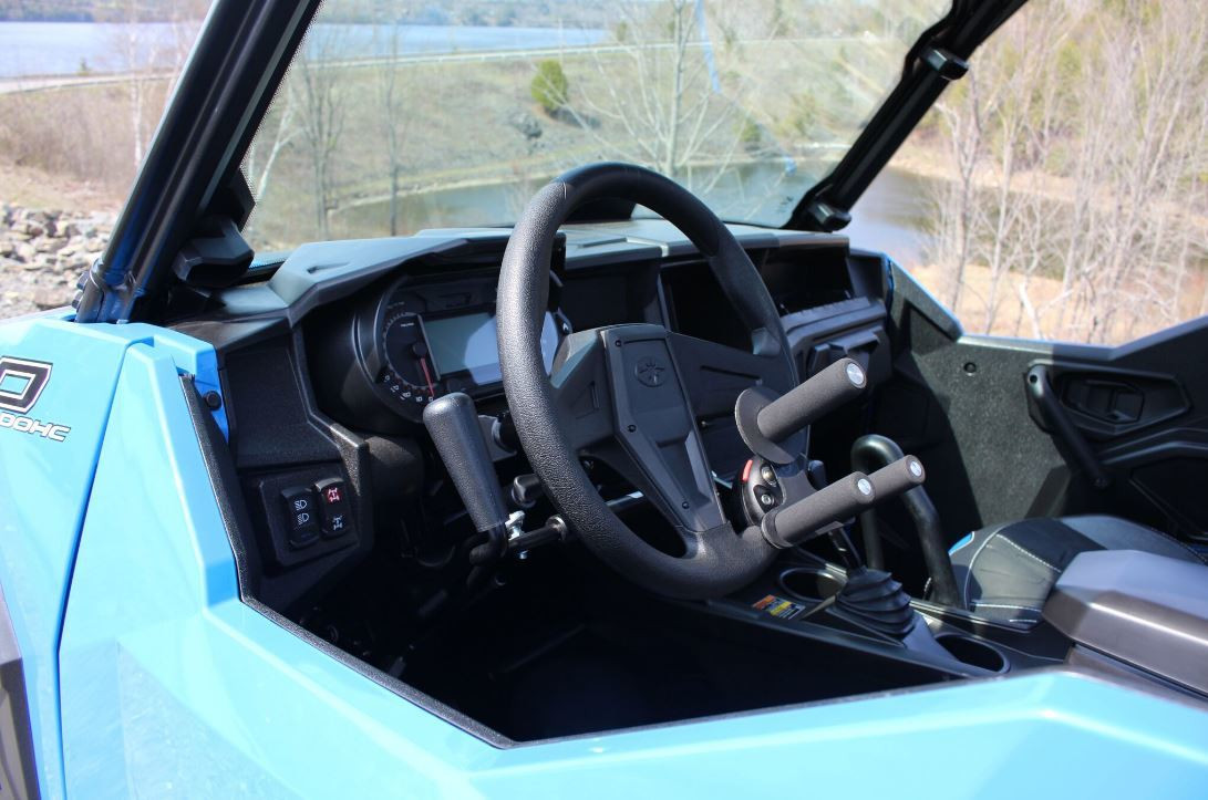 Sure Grip hand control lever mounted under the steering wheel of a blue side-by-side, seen through the driver door