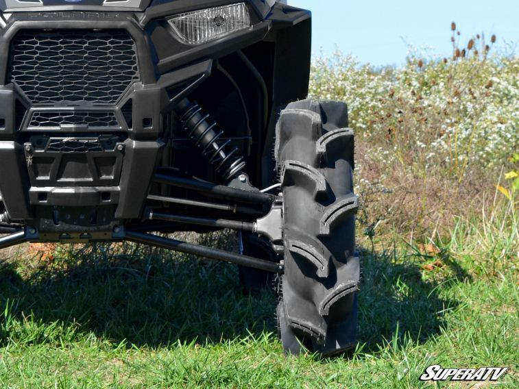 SuperATV Assassinator mud tire close-up on the front of a black side-by-side, showing deep angled lugs