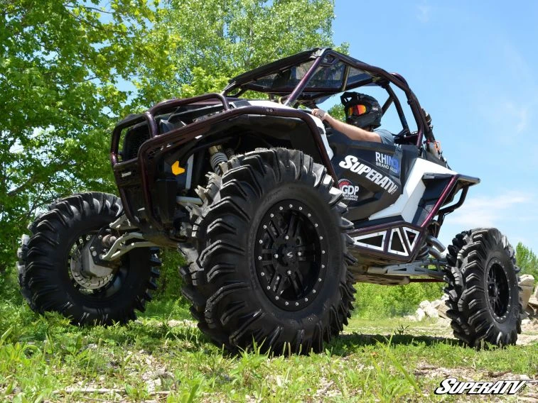 Black and white side-by-side on four SuperATV Terminator mud tires, rear three-quarter view on grass