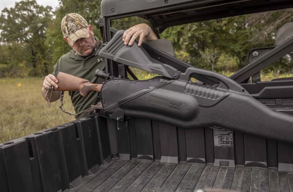 Hunter sliding a rifle into the Kolpin gun boot held by the InBed mount in the cargo bed of a Polaris Ranger