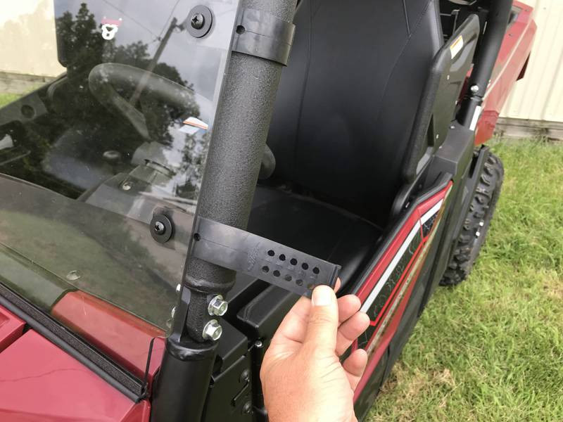 Hand pointing to the lower cage clamp of the Extreme Metal Products windshield on a red Yamaha Wolverine X2