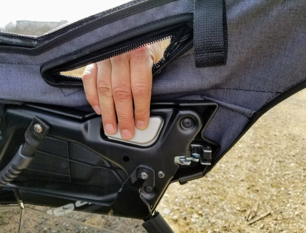 Hand gripping the pull strap on the Spike upper door showing the zipper and latch area on a RZR door