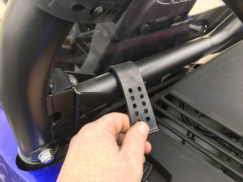Hand holding the rubber latch strap that secures the Extreme Metal Products dust stopper to the Yamaha YXZ roll cage
