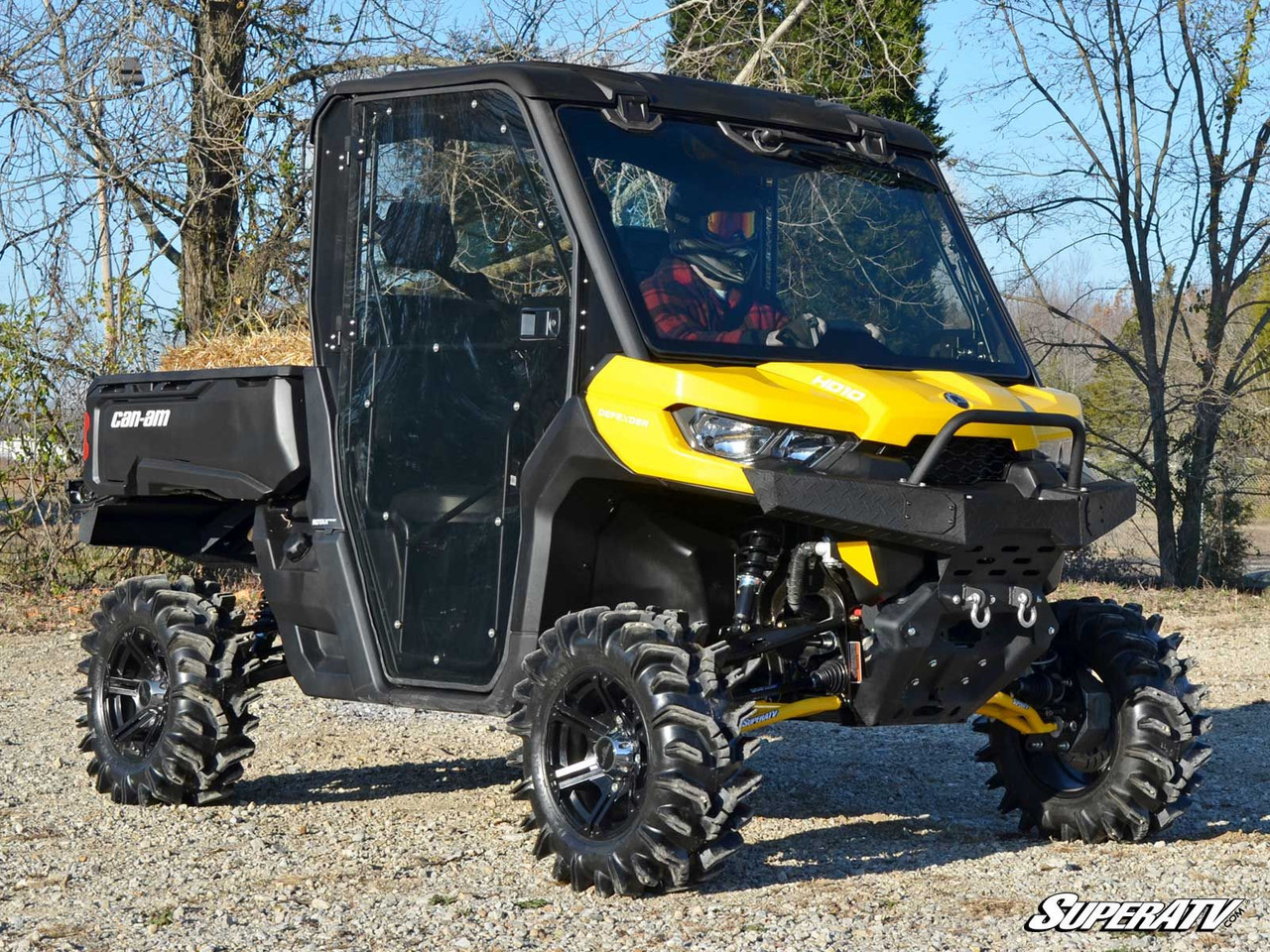 Yellow Can-Am Defender with full cab and the SuperATV diamond plate front bumper, side view on gravel