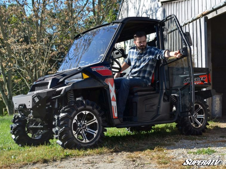 Driver climbing out of a Polaris Ranger with the SuperATV cab door swung open in front of a barn