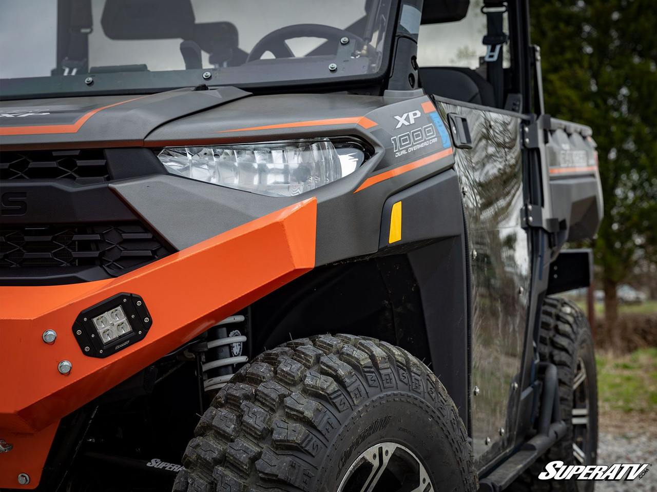 SuperATV recessed cube light flush mounted in the orange front bumper of a side-by-side, side angle by the headlight