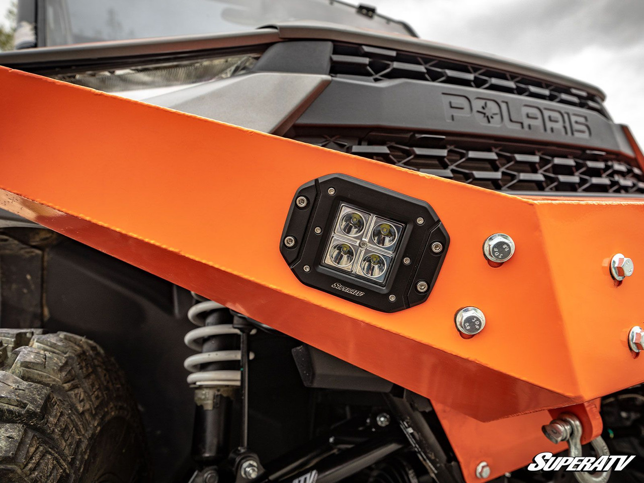 Close-up of a SuperATV 3-inch cube light recessed in an orange bumper below the grille of a side-by-side