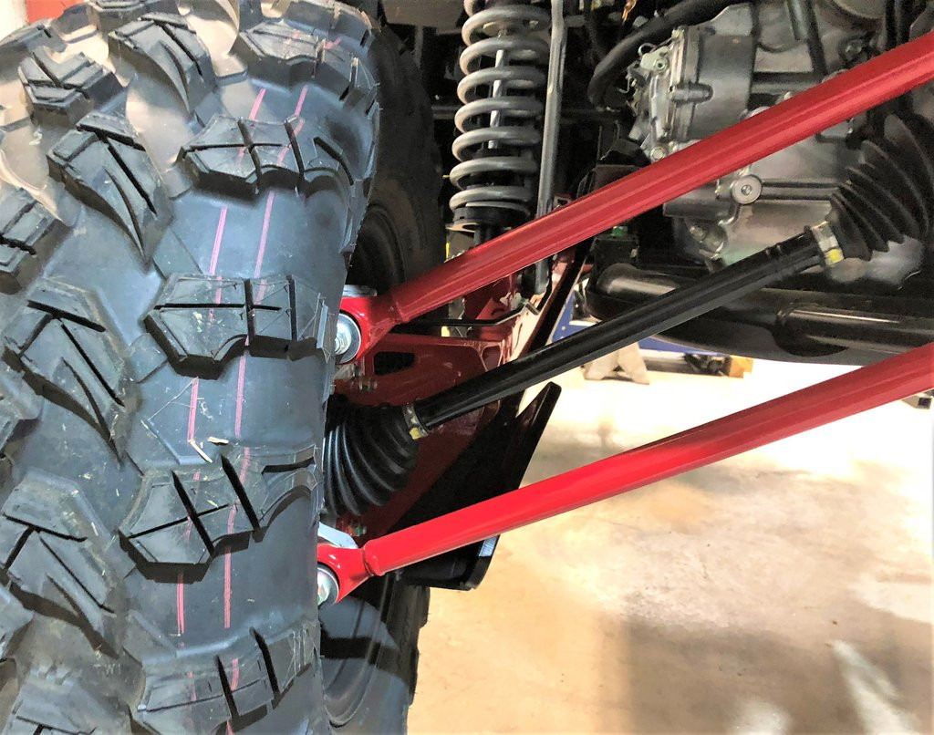 Trail Armor trailing arm guard beside the rear tire tread and shock of a Honda Talon 1000 X, close-up in a shop