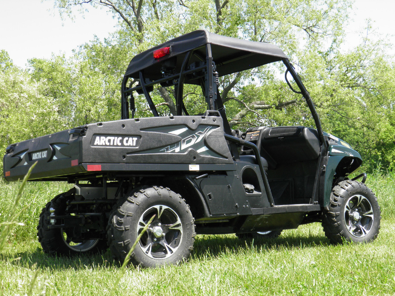 Rear three-quarter view of a black Arctic Cat Prowler 700 in a field with the 3 Star soft top over the cab
