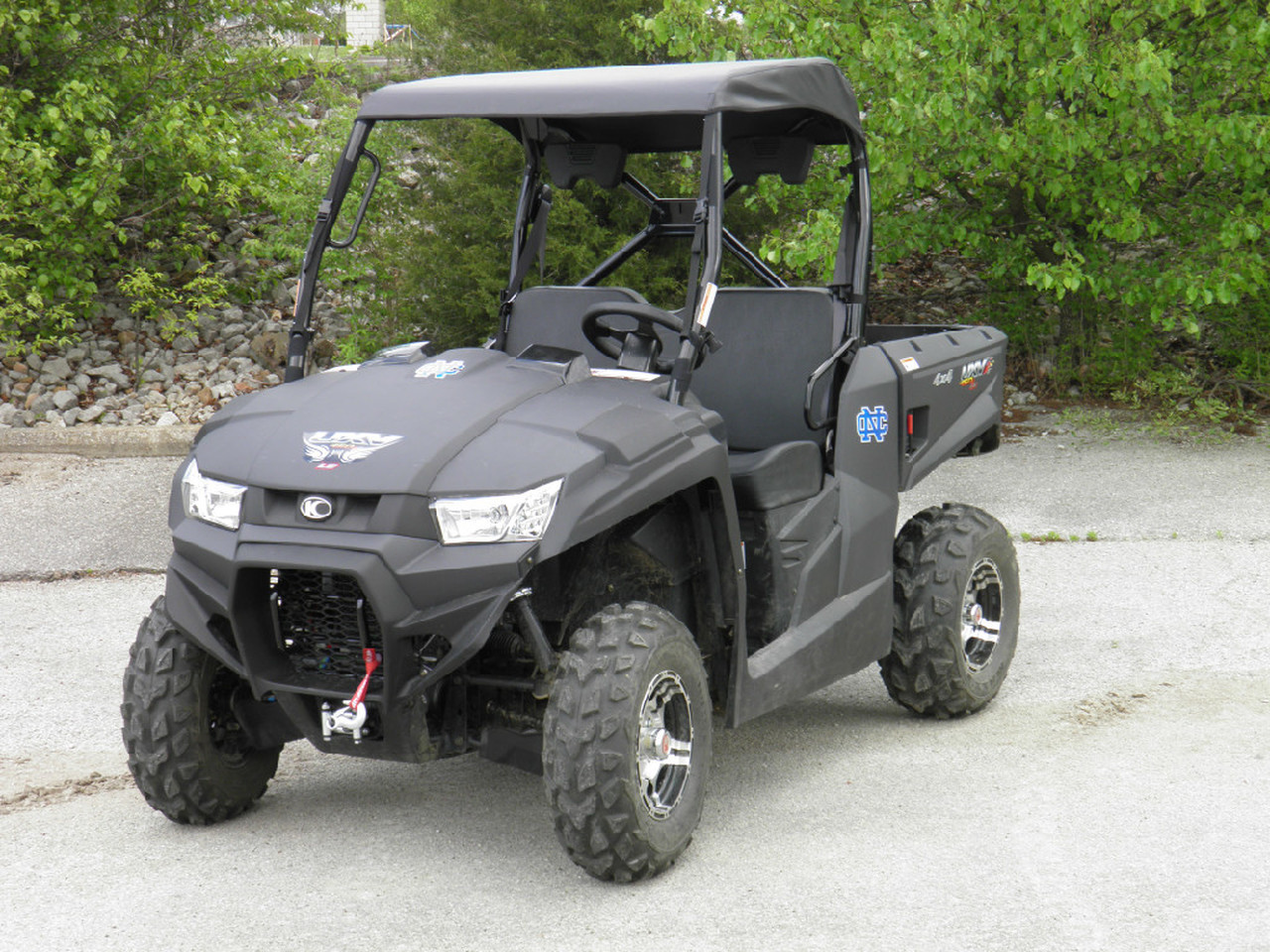 3 Star black soft top installed on a gray Kymco 450, front three-quarter view on gravel with trees behind