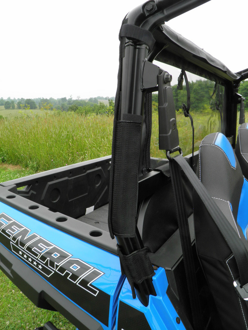 Close-up of the 3 Star soft back panel edge strapped to the rear cage tube of a blue Polaris General, side view