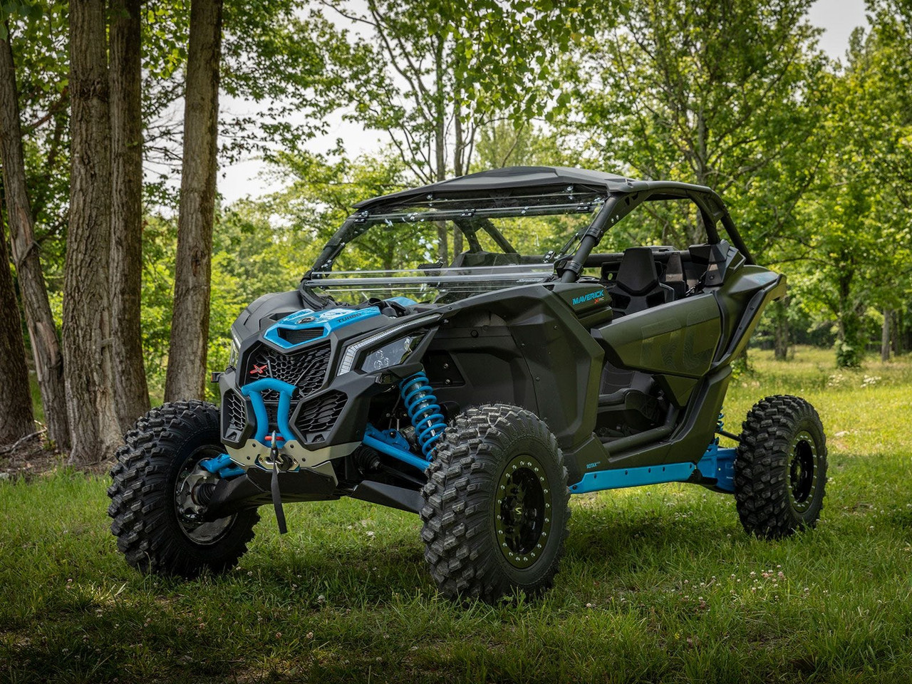SuperATV 3-inch lift kit installed on a green and blue Can-Am Maverick X3 parked among trees, front three-quarter view
