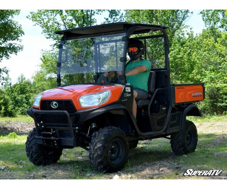 SuperATV 2 inch lift kit installed on an orange Kubota RTV X Series with roof, driven on a grass trail