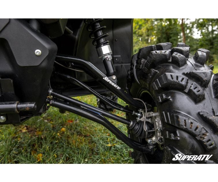Close-up of the lifted front suspension with SuperATV lift kit A-arms and shock behind a mud tire on the Defender
