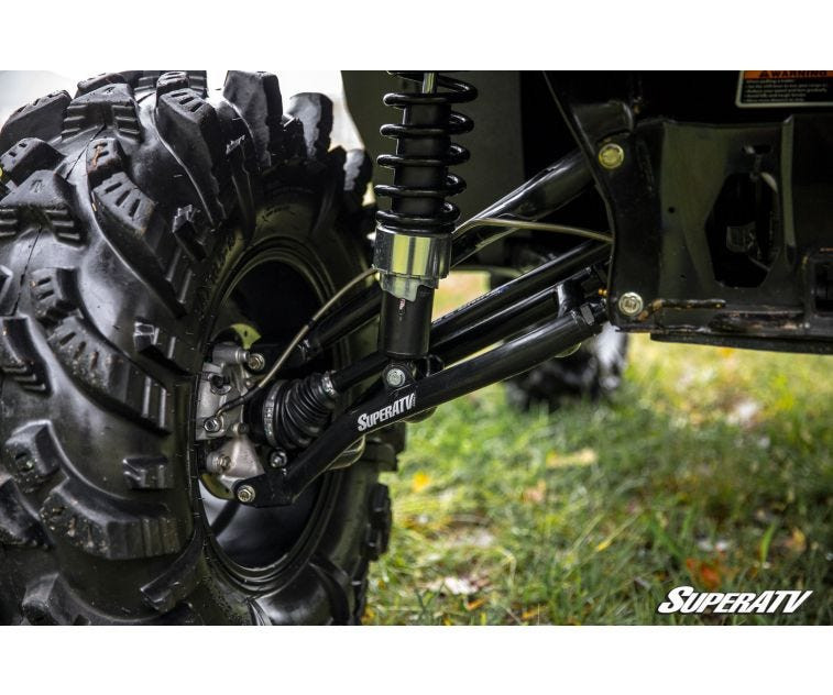 Close-up of the SuperATV lift kit control arm, shock and axle behind a mud tire on the Can-Am Defender