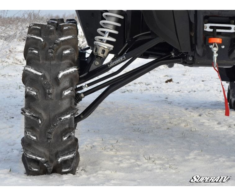 Close-up of the SuperATV front A-arms and coilover on a lifted Polaris RZR XP Turbo beside a mud tire