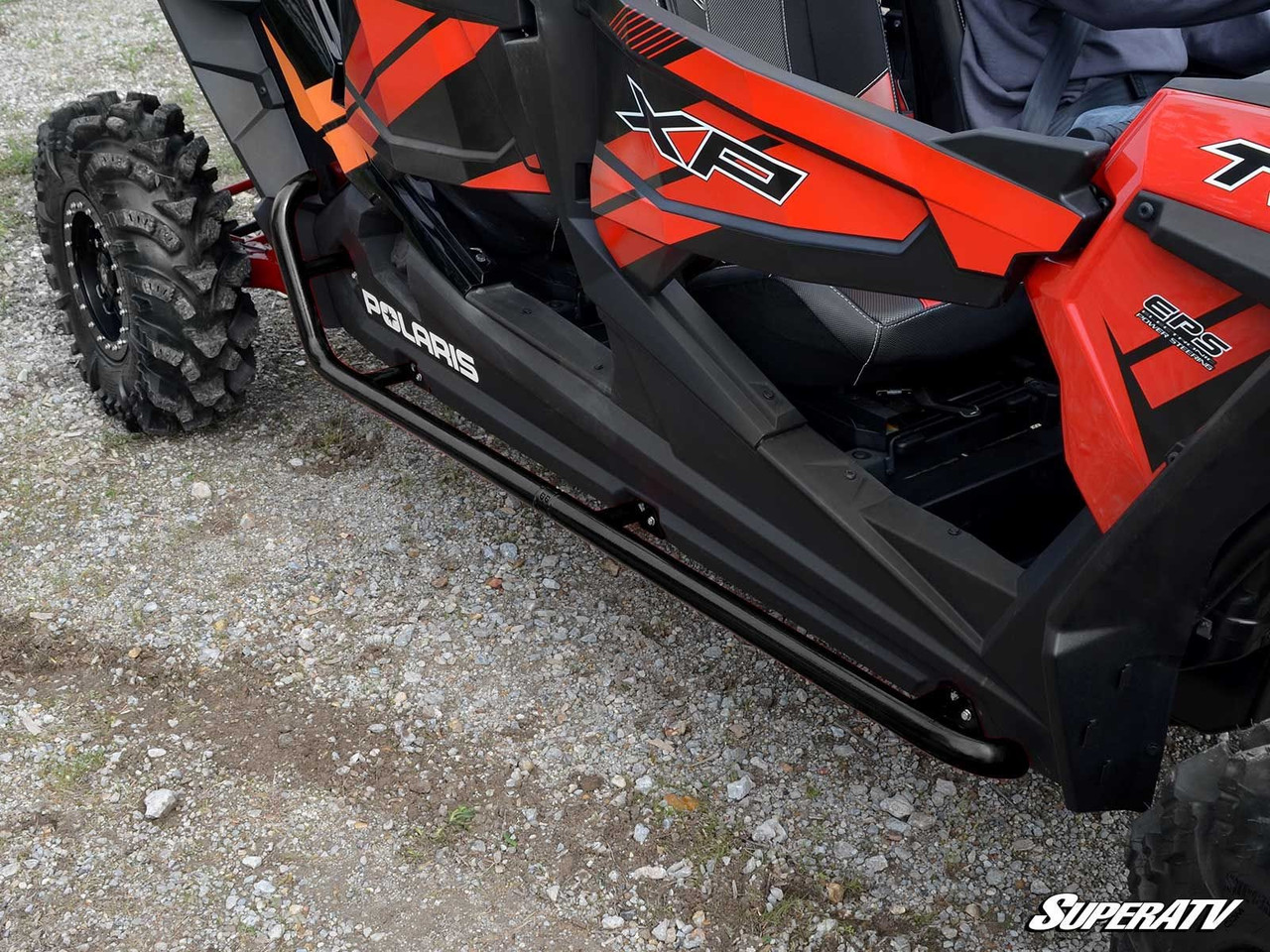Close-up of the SuperATV rock sliding nerf bar under the doors of an orange Polaris RZR XP 4 Turbo S on gravel