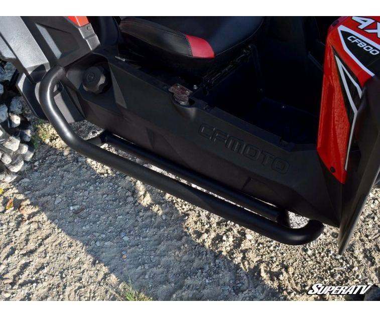 Close-up of the SuperATV heavy-duty nerf bar mounted on a red CFMoto ZForce rocker, parked on gravel