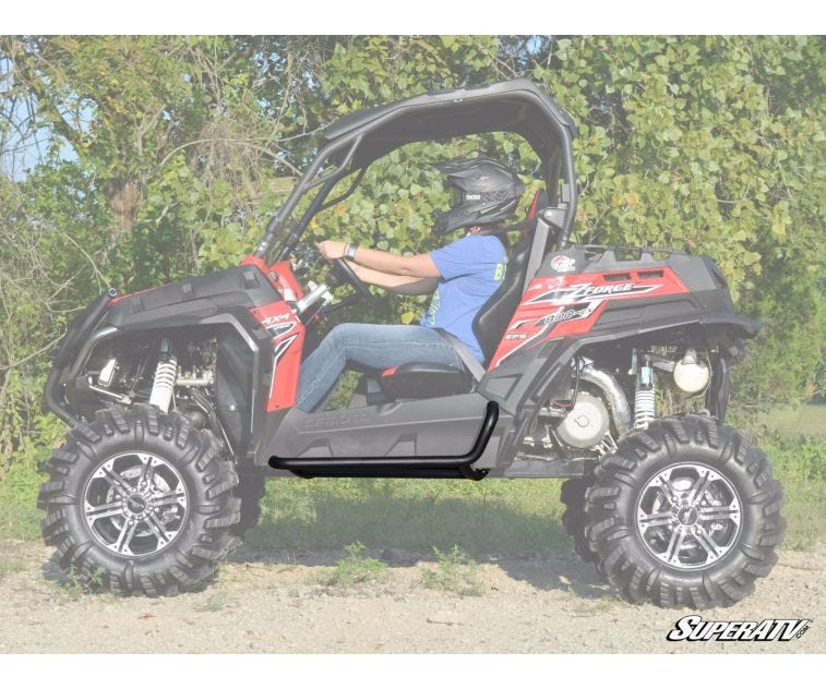 Red CFMoto ZForce with SuperATV heavy-duty nerf bars and a helmeted driver, full side view on a dirt lot
