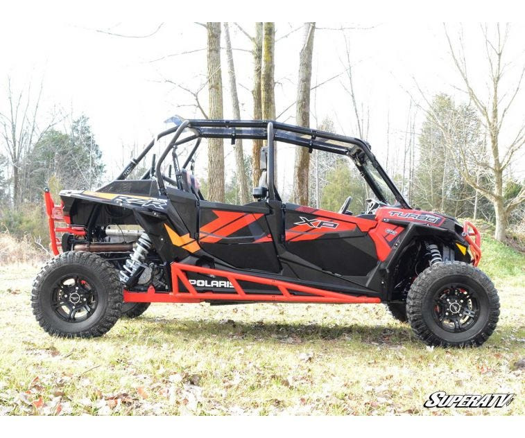 Side profile of a red four-seat Polaris RZR XP with SuperATV nerf bars along the rocker panels, on grass