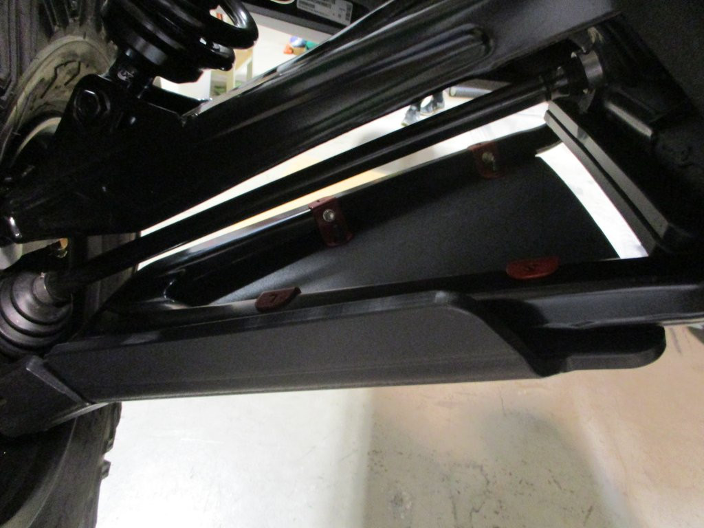 Trail Armor front impact guard installed under a Can-Am Maverick X3 lower A-arm, black UHMW panel with red push fasteners
