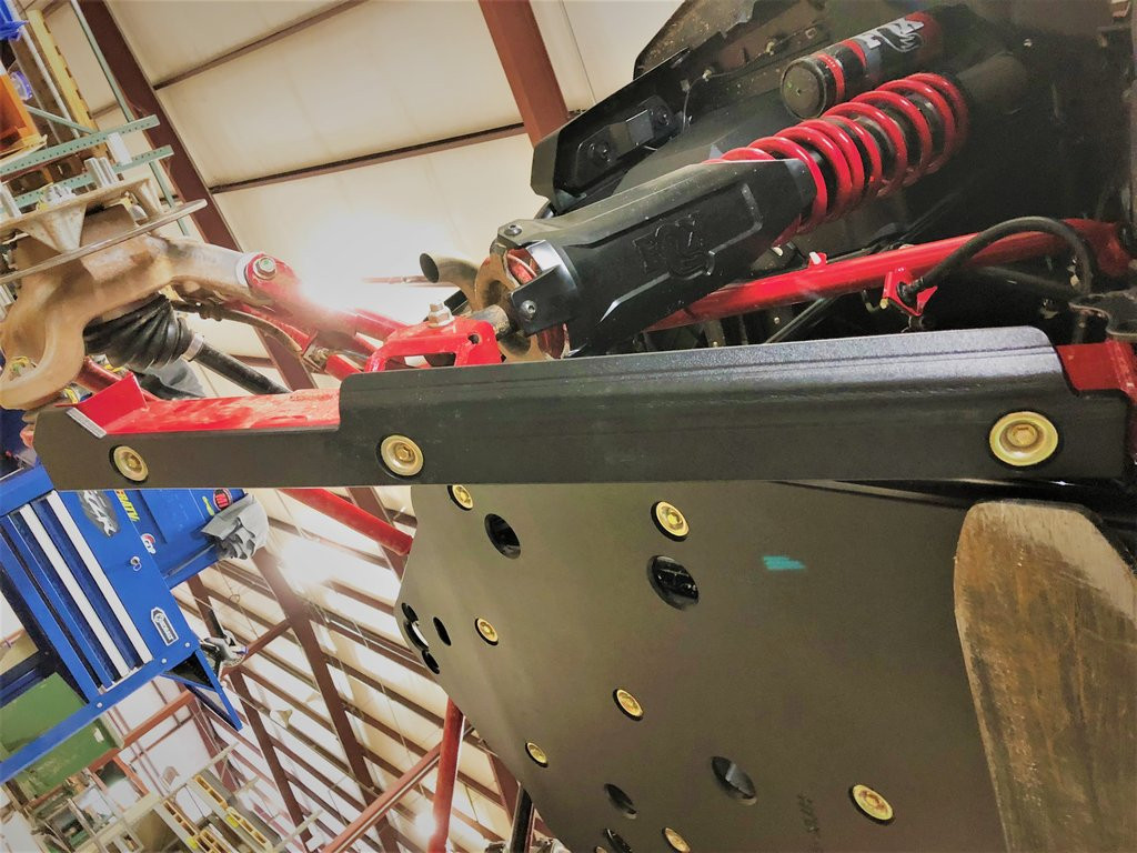 Trail Armor iMpact trailing arm guard installed on a red Kawasaki Teryx KRX rear arm, underside view in a shop