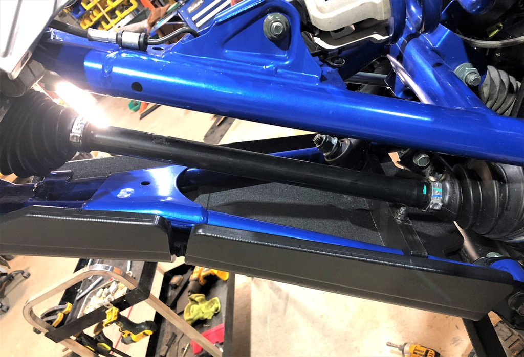 Trail Armor front arm guard on the blue Polaris RZR Pro XP A-arm viewed from below with the axle and tie rod