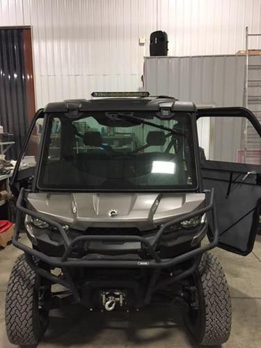 Universal Parts LED light bar mounted above the windshield of a gray Can-Am Defender with full cab, front view in a shop