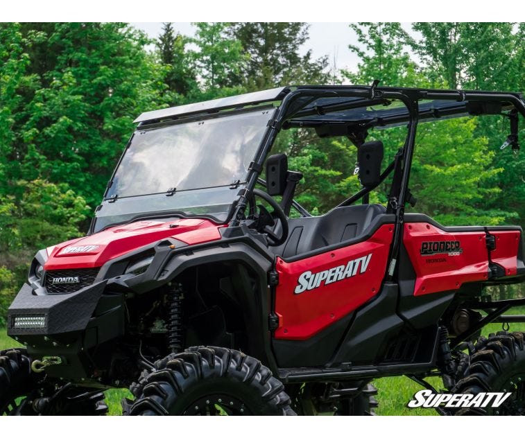 Close front three-quarter view of the SuperATV scratch resistant flip down windshield in place on a red Honda Pioneer 1000-5