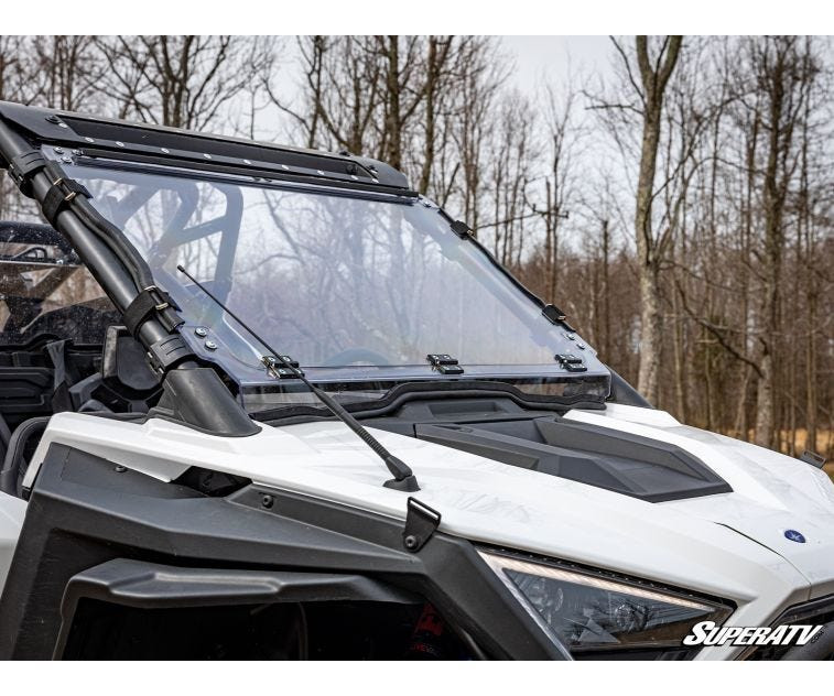 SuperATV flip down windshield in the closed position on a white Polaris RZR PRO XP, front three-quarter view in woods