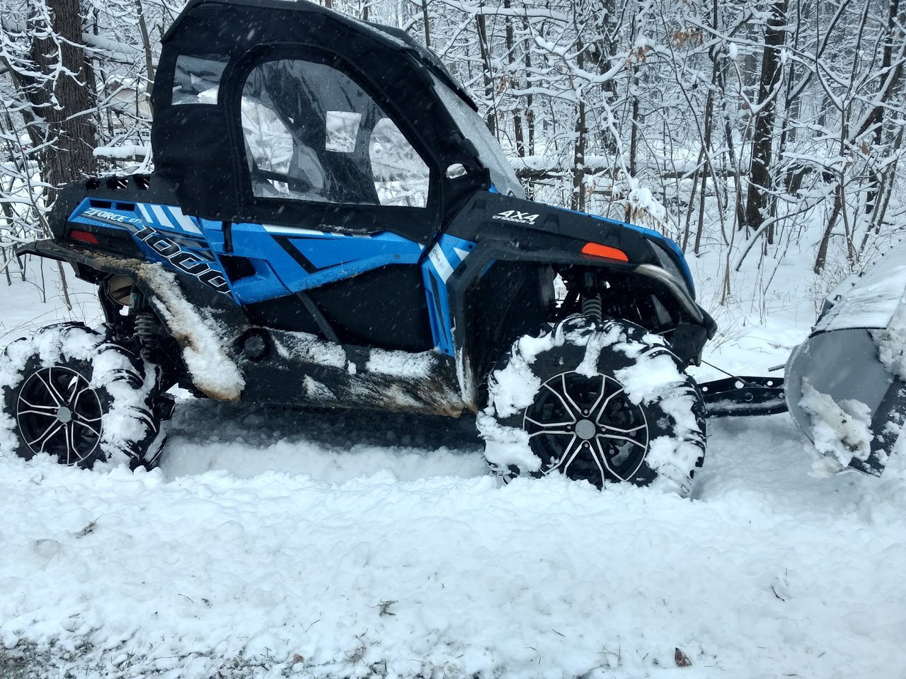 Side view of the blue CFMoto ZForce with Side X Side upper doors installed, pushing through deep snow