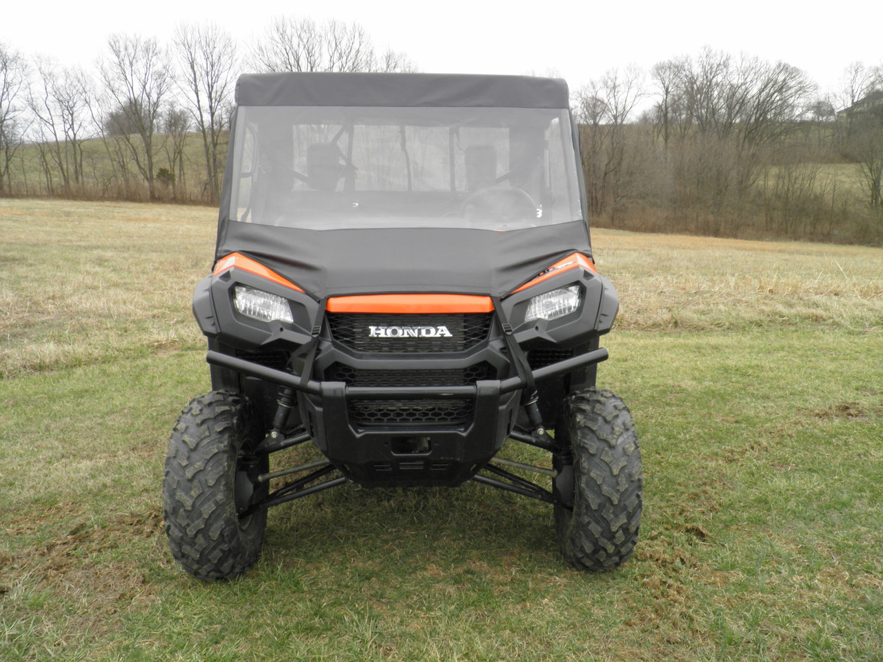 Front view of an orange Honda Pioneer 1000 wearing the 3 Star vinyl windshield and black soft top in a field