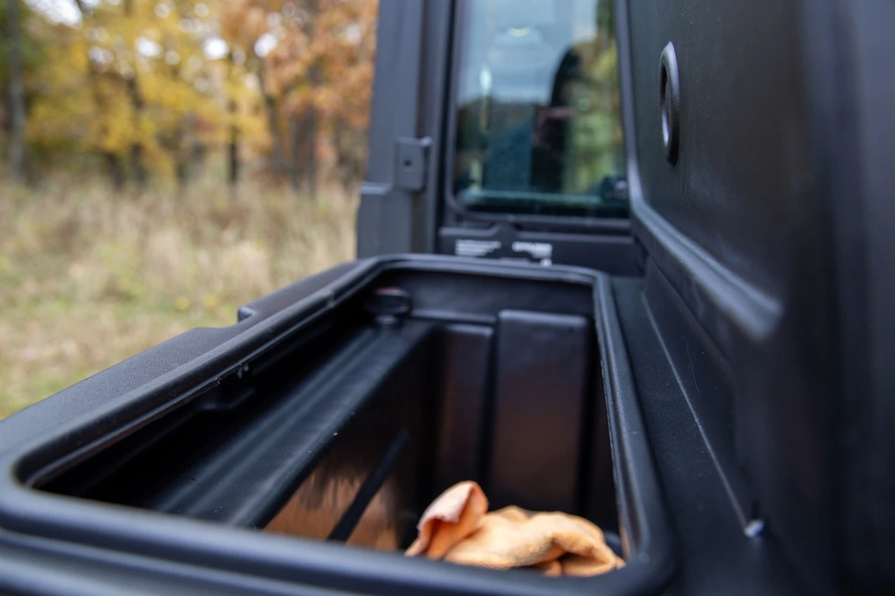 Looking down into the open Kolpin saddle storage box behind a Polaris Ranger cab, a pair of gloves in the tub