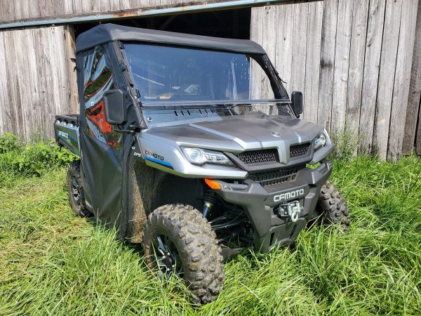 Front three-quarter view of a gray CF Moto UForce 1000 with the 3 Star full cab enclosure by a barn