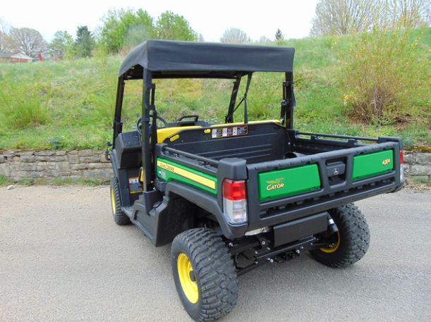 Rear three-quarter view of the 3 Star soft top on the John Deere Gator above the cargo bed, parked by a grass bank