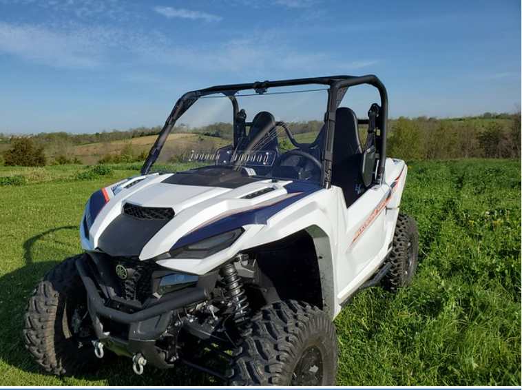 Low front three-quarter view of a white Wolverine RMAX with the 3 Star one-piece windshield, sky and treeline behind
