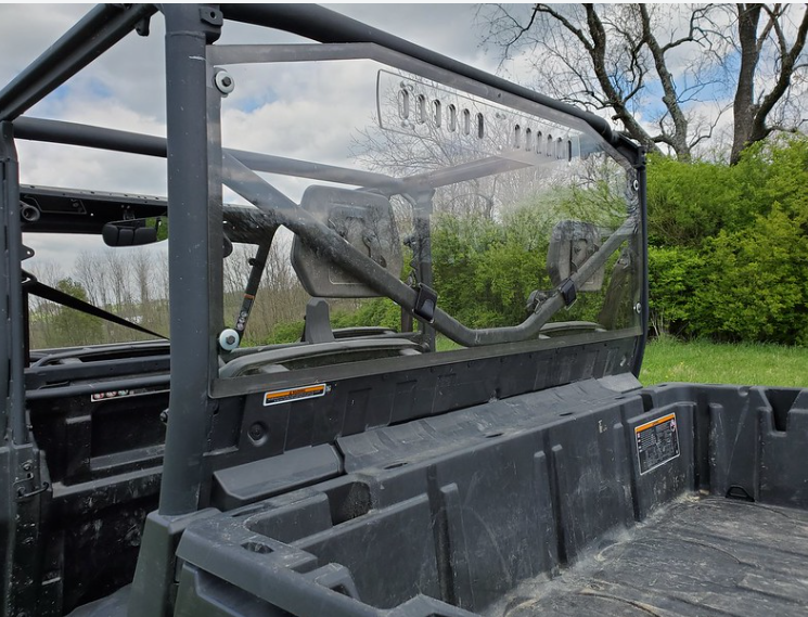 Angled view from the bed of the 3 Star Lexan rear window on a Can-Am Defender Max showing the cage clamps and vents