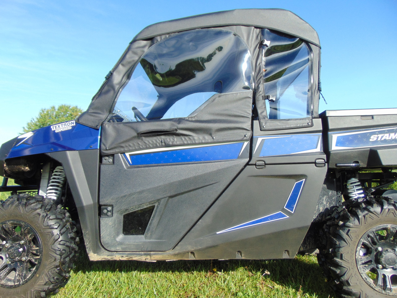 Driver side close-up of the 3 Star soft door and window on a blue Arctic Cat Stampede on grass