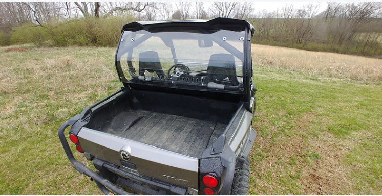 Rear three-quarter view of the 3 Star Lexan rear window on a gray Can-Am Commander in a field, cargo bed and taillights below