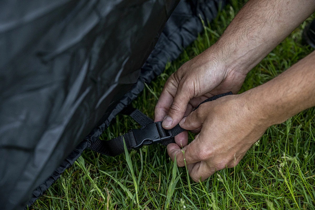 Close-up of the Kolpin UTV cover cinch strap buckle being fastened near the ground, grass below