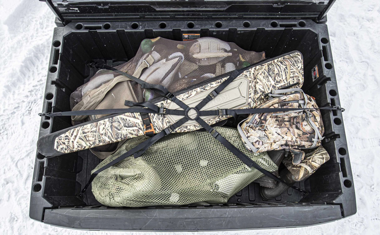 Kolpin cargo spider strap securing camo hunting gear in a UTV bed, viewed from above