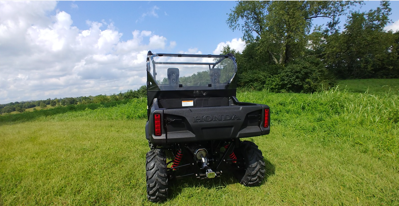 Rear three-quarter view of the black Honda Pioneer 700 with the 3 Star Lexan rear window, wide shot in a field