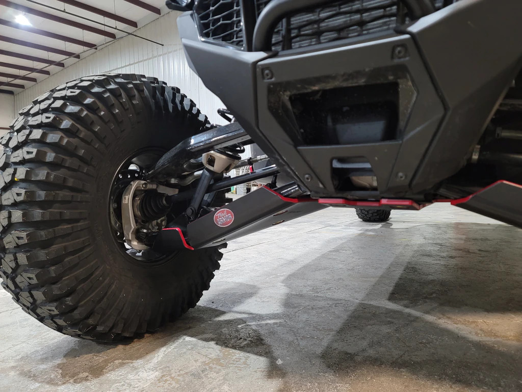 Front corner view of the Trail Armor arm guard under a Polaris RZR Pro R front A-arm beside the knobby tire