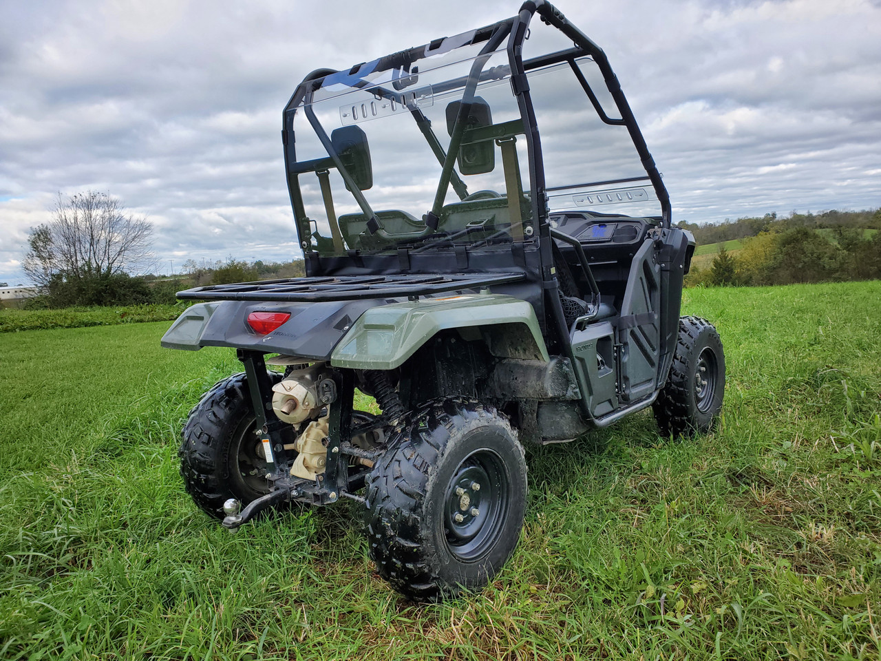 Driver side rear three-quarter view of a green Honda Pioneer 500 with the 3 Star Lexan rear window in the cage