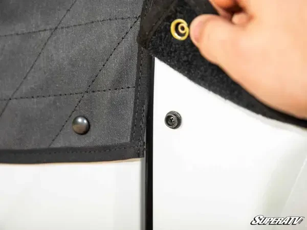 Close-up of a hand lifting the hook-and-loop flap and snap that secure the SuperATV soft door to the lower door