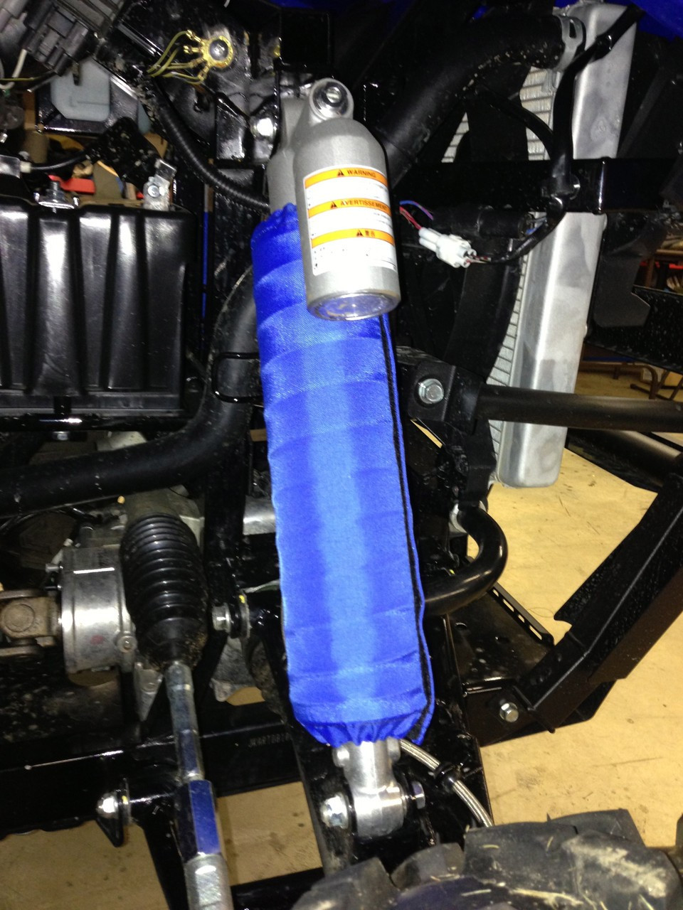 Greene Mountain blue shock cover installed on a rear shock of a Kawasaki Teryx, close-up in a shop