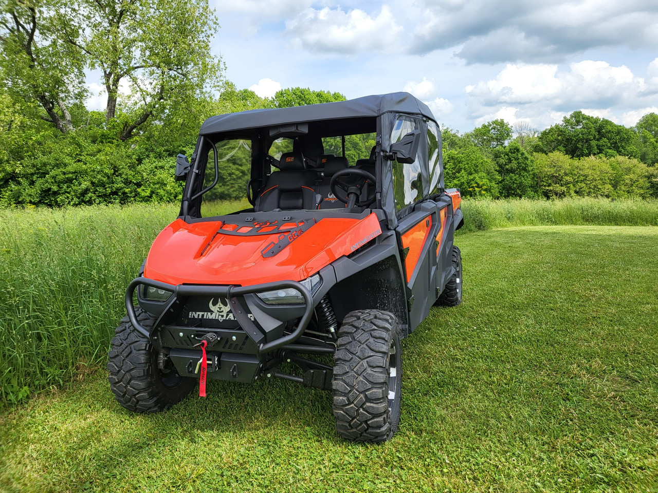 Front three-quarter view of the orange Intimidator GC1K with the 3 Star full cab enclosure, trees behind